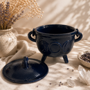Navy blue ceramic cauldron with a lid on a textured surface with decorative elements.