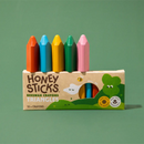 Box of Honey Sticks beeswax crayons with colorful crayons on a green background