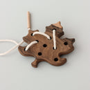 A wooden toy shaped like a leaf with lacing holes and a white string.