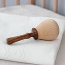A wooden rattle crafted from Linden wood, with a handle and filled with dried peas, lying on a white cloth.