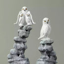 Two stone sculptures of snowy owls on gray rock bases against a gray background