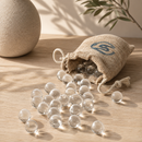 Clear glass marbles spilling out of a jute bag with a logo on a wooden surface.