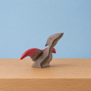 Wooden figurine of a stylized creature with red accents on a wooden surface and blue background