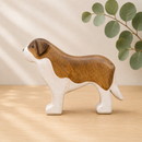Wooden dog figurine on a wooden surface with a beige background and green leaves.