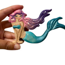 A wooden mermaid toy with painted features and a tail, held in a person's hand.