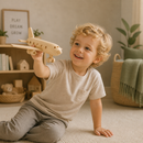 Child holding a wooden airplane toy in a cozy room with plants and shelves.