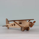 A wooden toy airplane with a two-tone design, featuring a lighter wood fuselage and darker wood wings and propeller, placed on a flat surface.