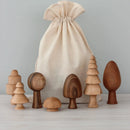 A set of wooden toy trees in various shapes and sizes displayed in front of a beige drawstring bag on a light background.