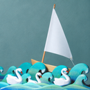 Styled scene featuring the Bumbu Toys white sailing boat behind teal wooden waves and three swan figures.