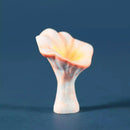 A small sculptural flower-shaped object with pale pink petals, a warm yellow center, and a white stem, photographed against a dark blue background.