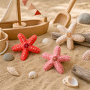 Starfish toys on sand with a wooden sailboat and shells