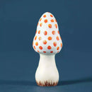 A small mushroom-shaped decorative object with a white body and orange polka dots on the cap, standing on a dark blue background.