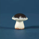 A small mushroom figurine with a dark brown cap and an off-white stem, standing on a matching dark blue surface.