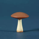 A small mushroom figurine with a brown cap and a cream-colored stem with brown speckled detailing, standing on a blue surface against a blue background.