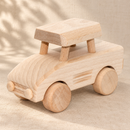 Bartu Minny natural wooden toy car facing left at a front three-quarter angle on a warm beige textured surface.