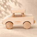 Side view of the Bartu Minny natural wooden toy car facing left on a warm beige textured surface.