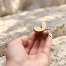Oshkin wooden fly with pale wooden wings and thin dark wire legs, held in a hand against a softly blurred stone background.