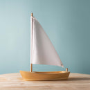Bumbu Toys wooden sailing boat with a white fabric sail and natural wood hull.