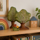 Wooden toys including trees, a rainbow, and a house on a shelf with books and a plant.