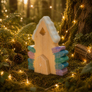 Wooden fairy house with colorful stacked stones in a forest setting with fairy lights.